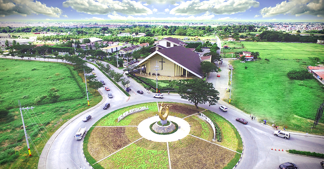 Aerial drone view of Lancaster New City rotunda in Imus, Cavite — showing community roads, green spaces, and the Parish of the Holy Family church